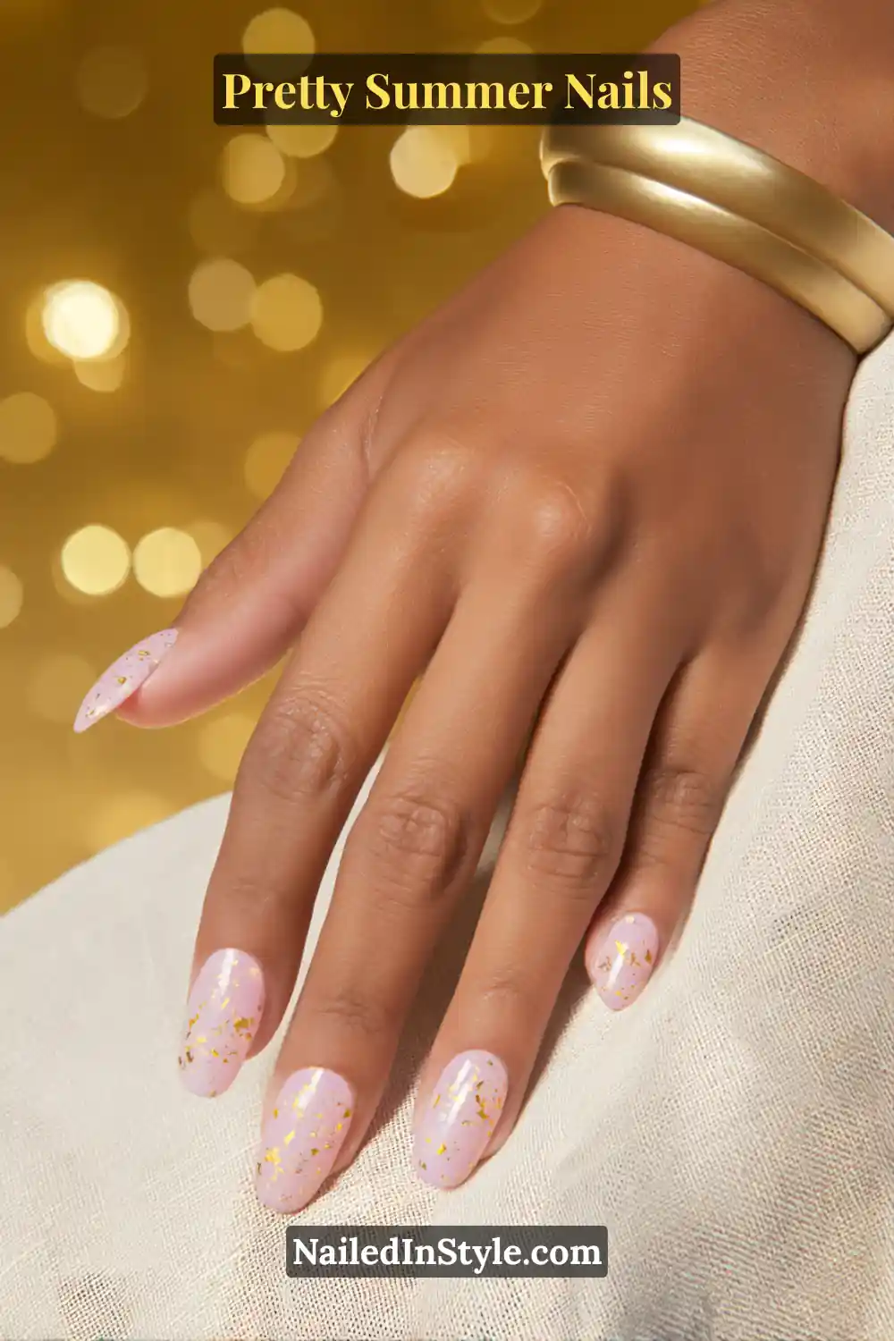 Hand with oval-shaped nails painted in soft rose quartz pink, decorated with subtle gold flecks, complementing medium skin tones.