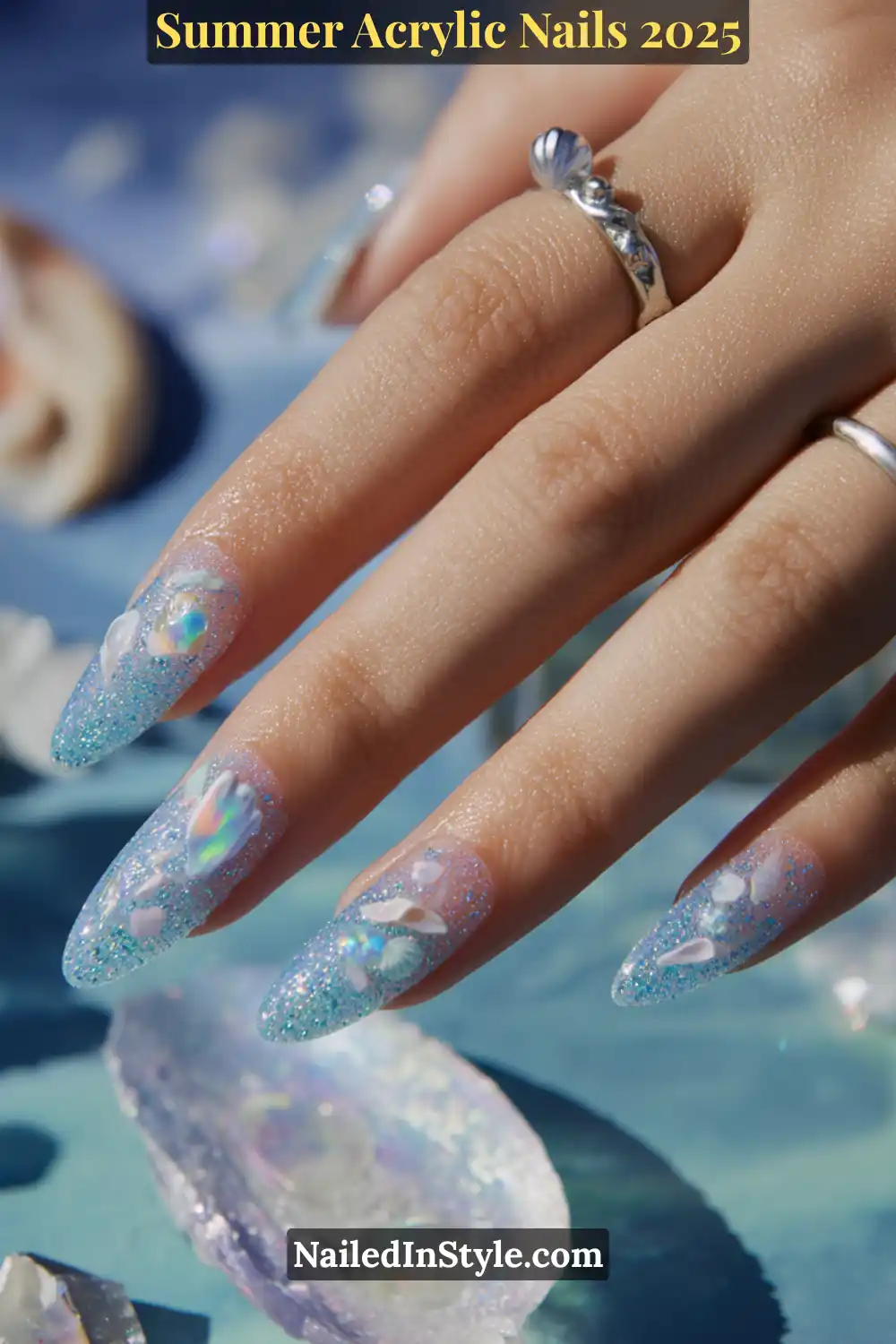 Summer Acrylic Nails 2026: Bold, Beautiful & Built to Last 3 Hand with almond-shaped acrylic nails featuring aqua blue glitter base, iridescent shell-like decals, and 3D sea-inspired accents