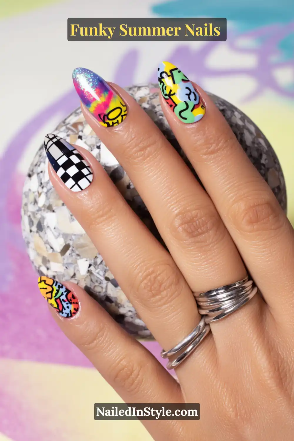 Hand with nails featuring different funky designs on each nail: checkerboard, tie-dye, doodle art, glitter, and abstract patterns in bold summer colors.