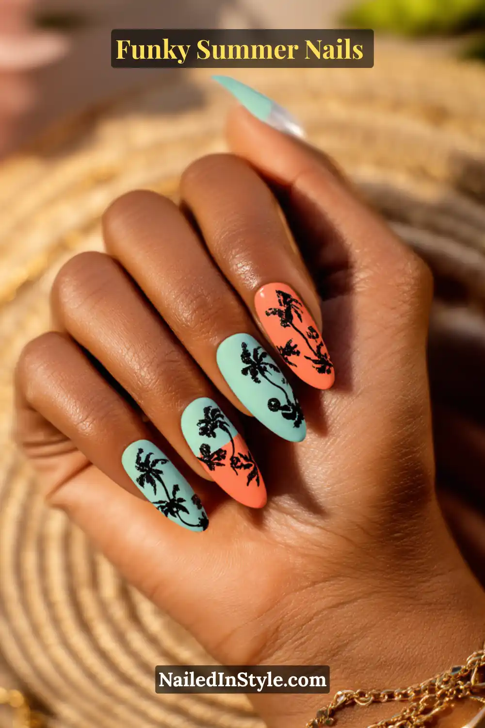 Hand with long almond nails painted in matte aqua blue and coral orange, decorated with black palm tree silhouettes. A tropical beach-inspired funky nail design.
