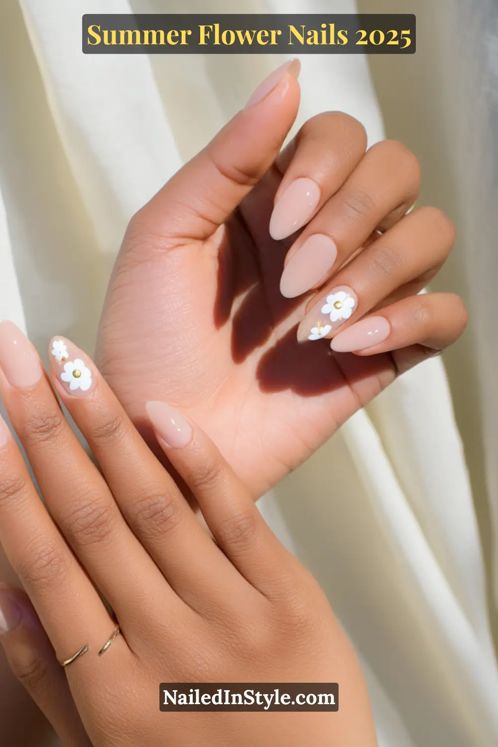 Almond-shaped nails painted in peachy nude with white daisy floral accents on the ring fingers.
