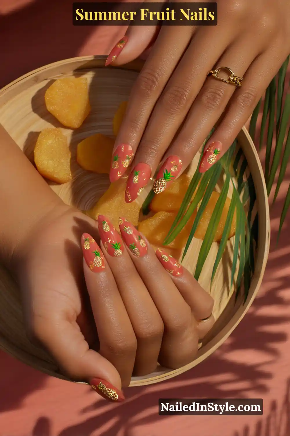 Almond-shaped nails with a coral base and intricate golden pineapple designs.