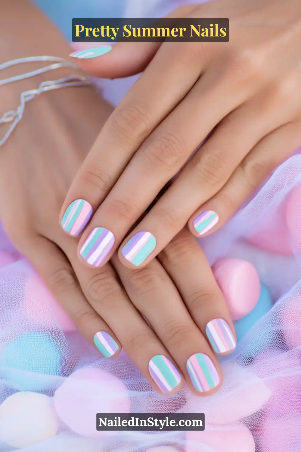 Hand with short almond-shaped nails painted in mint, baby blue, and lavender pastel stripes, styled against soft pastel fabric.