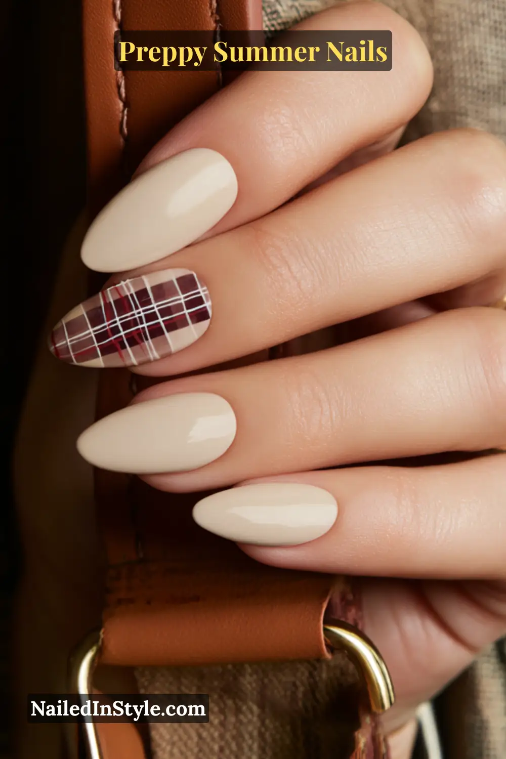 Hand with nude almond nails featuring one accent nail in burgundy plaid pattern.