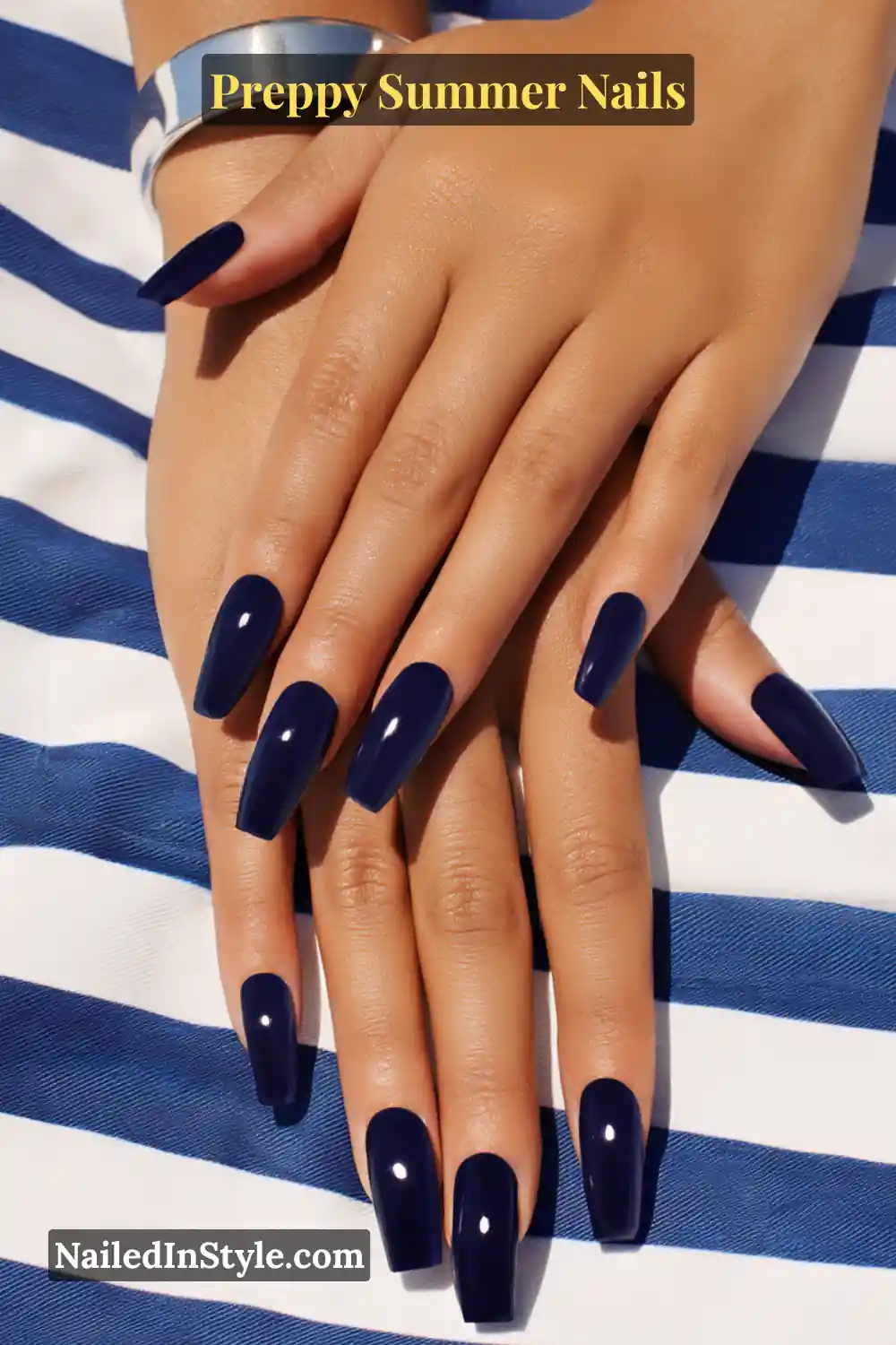 Hands with long, glossy deep navy blue polished nails against striped fabric.