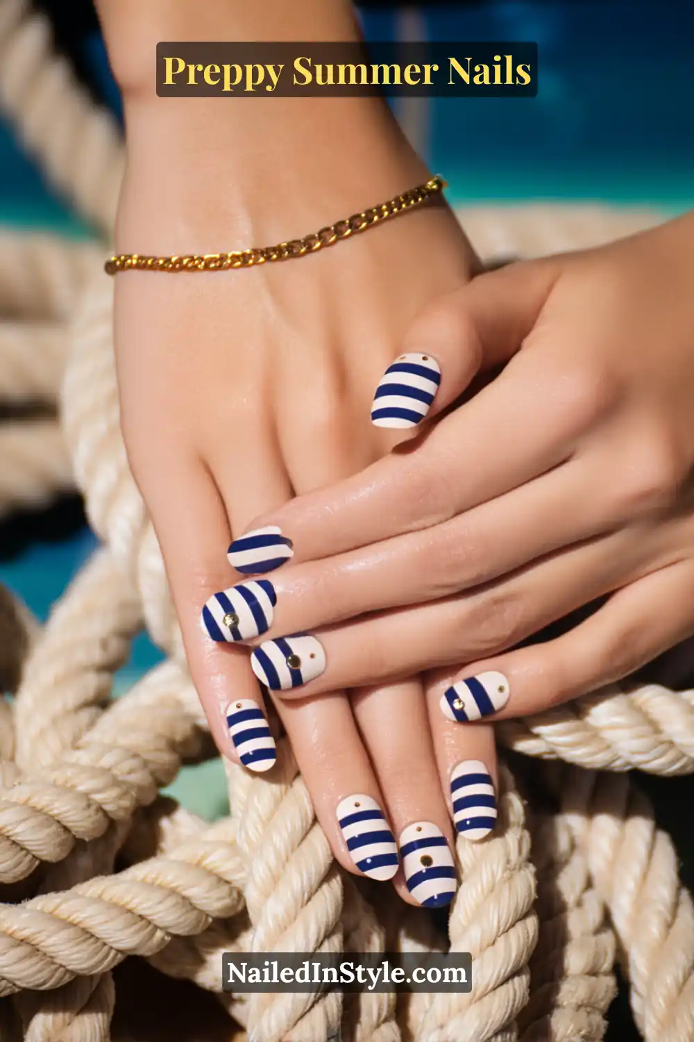 Hands with cream nails featuring bold navy horizontal stripes and small gold accent dots.