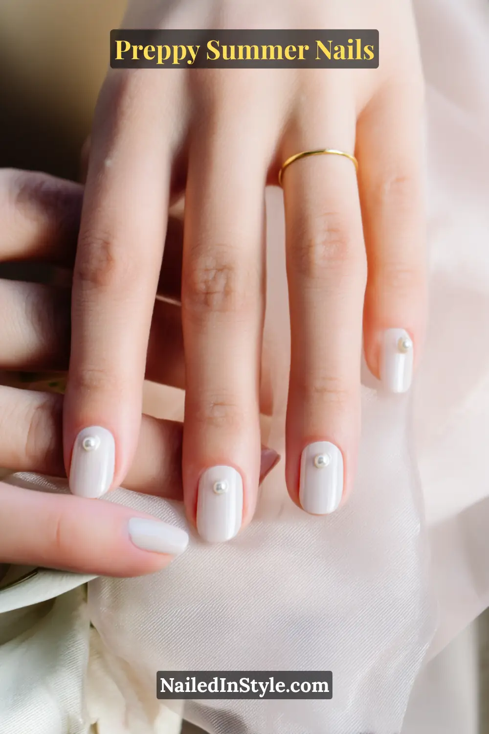 Hands with glossy nude-white nails, each featuring a delicate single pearl embellishment.
