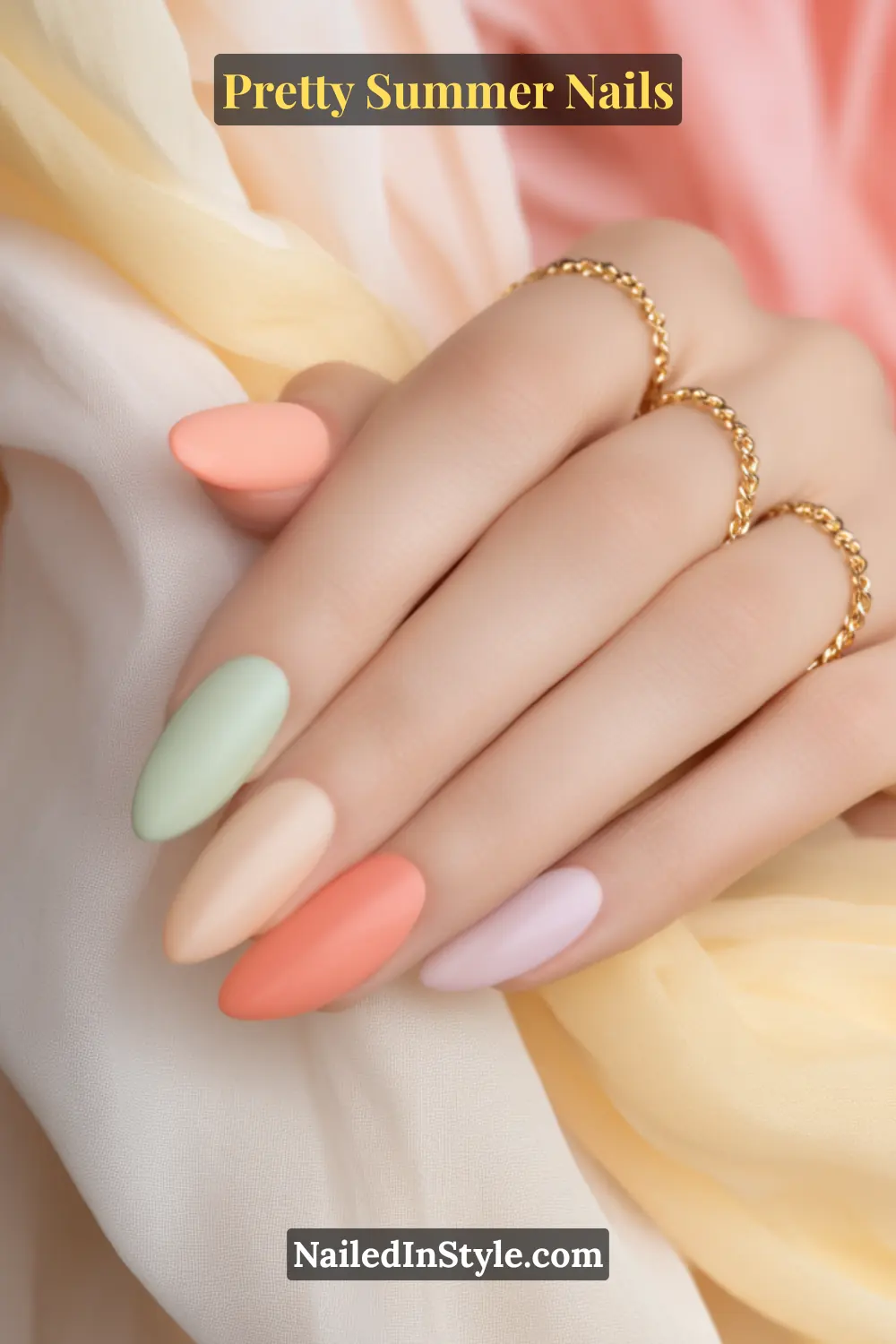 Pretty Summer Nails Hand with almond-shaped nails painted in soft pastel shades—peach, mint, cream, coral, and lilac—styled against flowing fabric with gold rings.