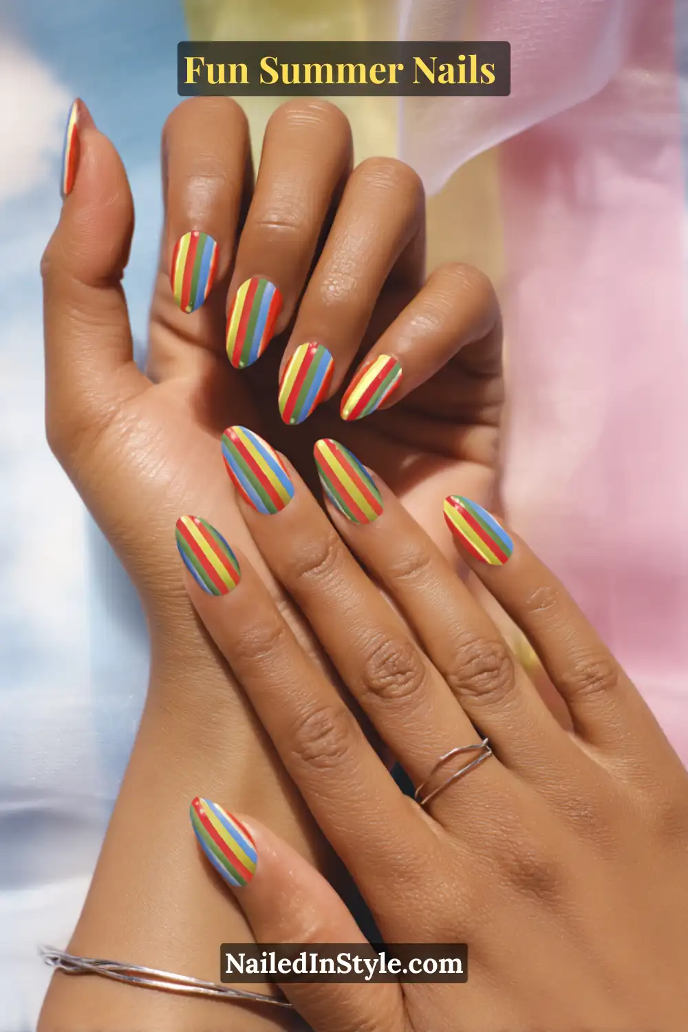 Hands with rainbow stripe nails featuring vertical red, yellow, green, and blue lines on a glossy base.