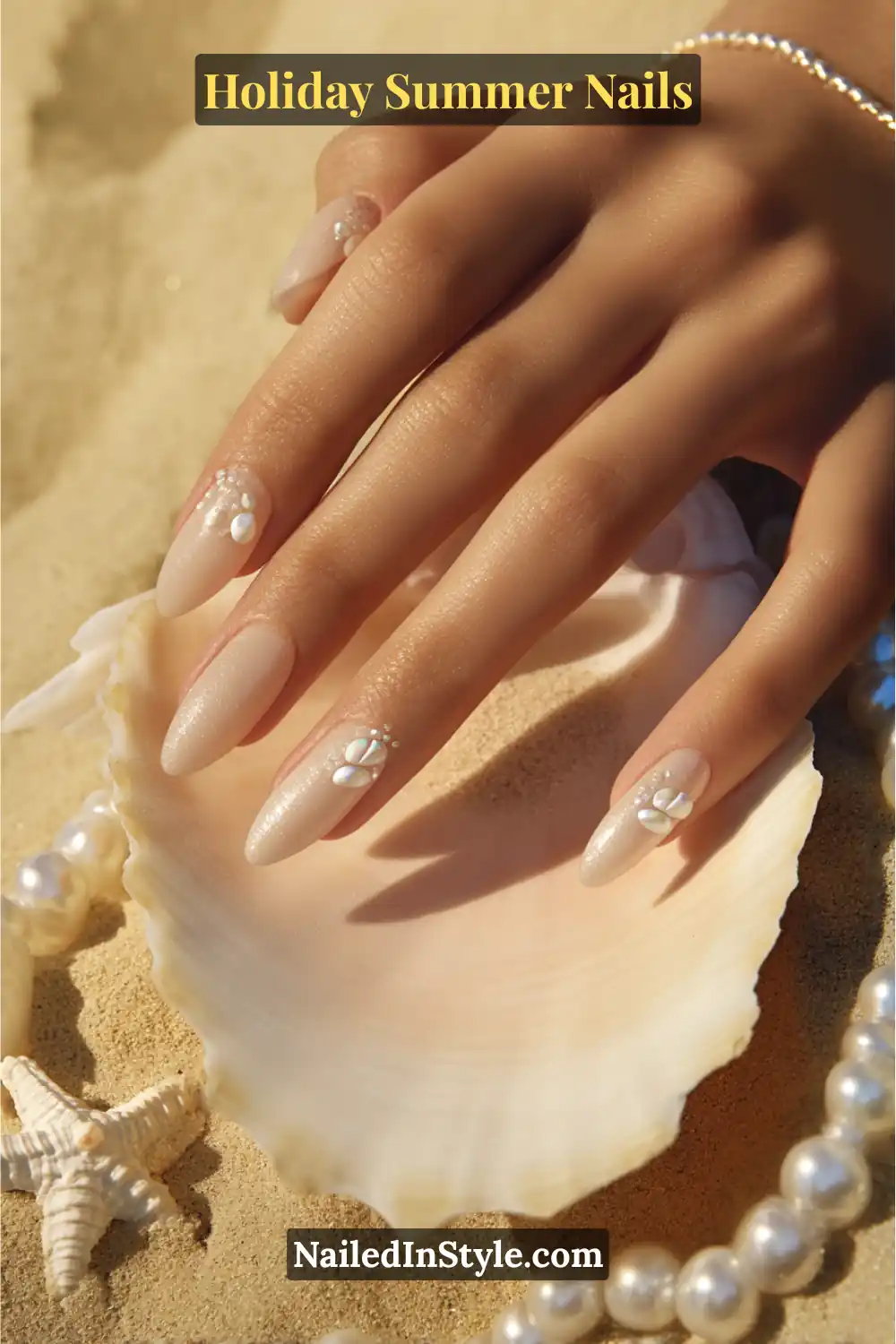 Elegant nude pearl nails with 3D seashell accents and pearls, styled on sandy beach background.
