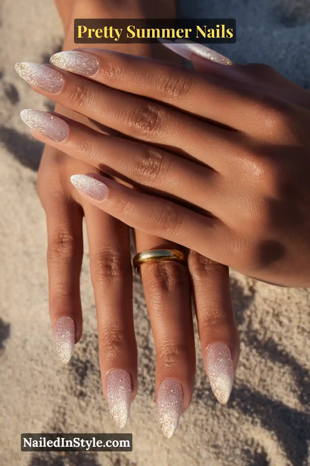 Close-up of hands with almond-shaped nude nails featuring a champagne gold glitter fade at the tips.