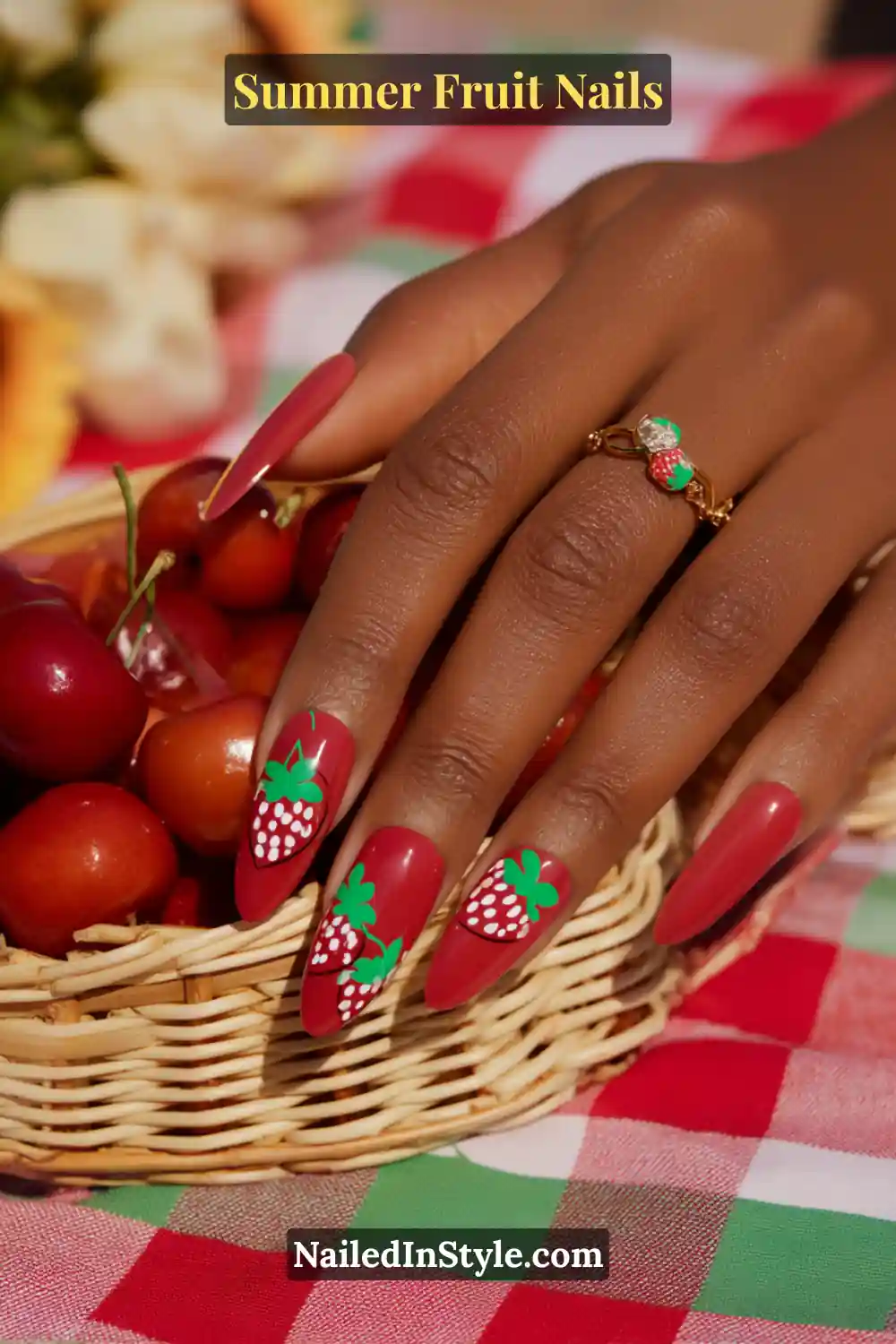 Almond-shaped nails in deep matte red with playful strawberry nail art in green and white.