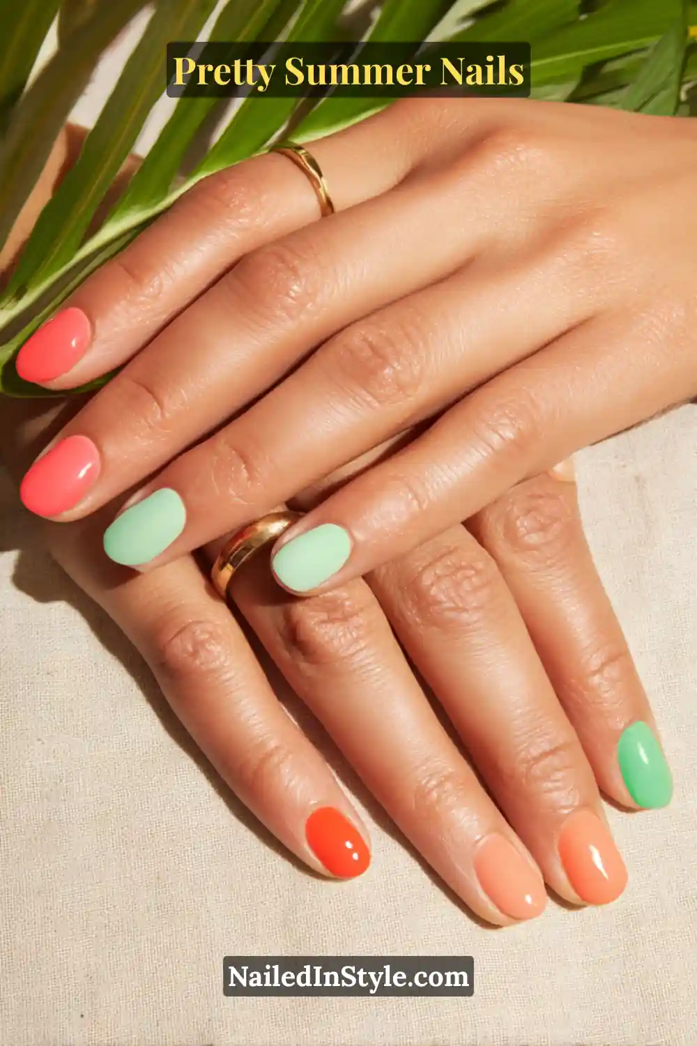 Hands with nails painted in alternating coral, mint green, and peach tones, creating a fresh summer look that enhances tan skin.