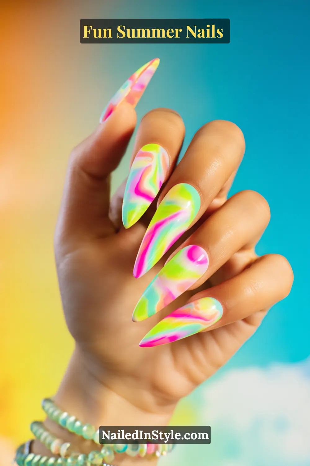 Hand with long stiletto nails in bright multicolor tie-dye swirls of pink, green, yellow, and blue.
