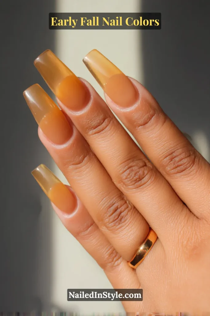 Early fall nail colors in translucent amber glass style with a warm honey glow, photographed in natural backlight.