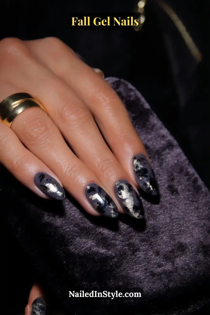 fall gel nails in black with silver foil specks, oval shape, hand resting on velvet pouch
