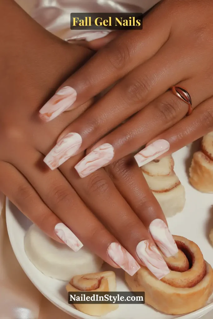 fall gel nails in nude marble design with caramel swirls, coffin shape resting over a pastry plate with cinnamon rolls