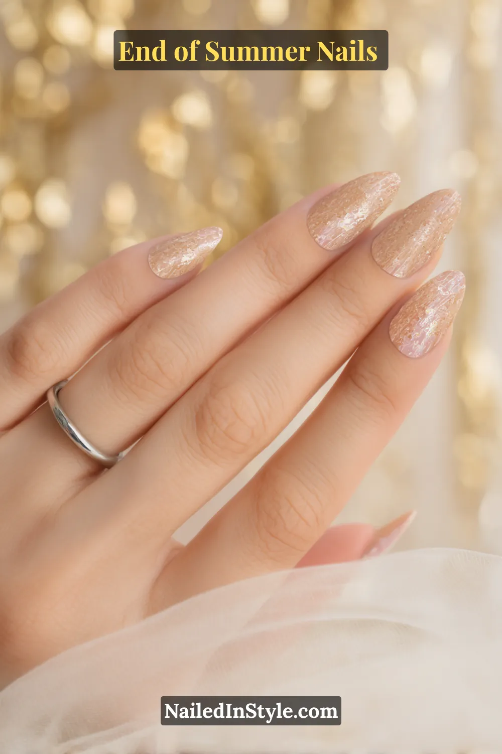 Close-up of a hand with almond-shaped nails painted in a neutral beige base with shimmering champagne glitter overlay.