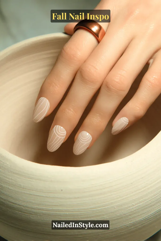 Beige nails with fine white spiral line art at the cuticle, resembling pottery coils.