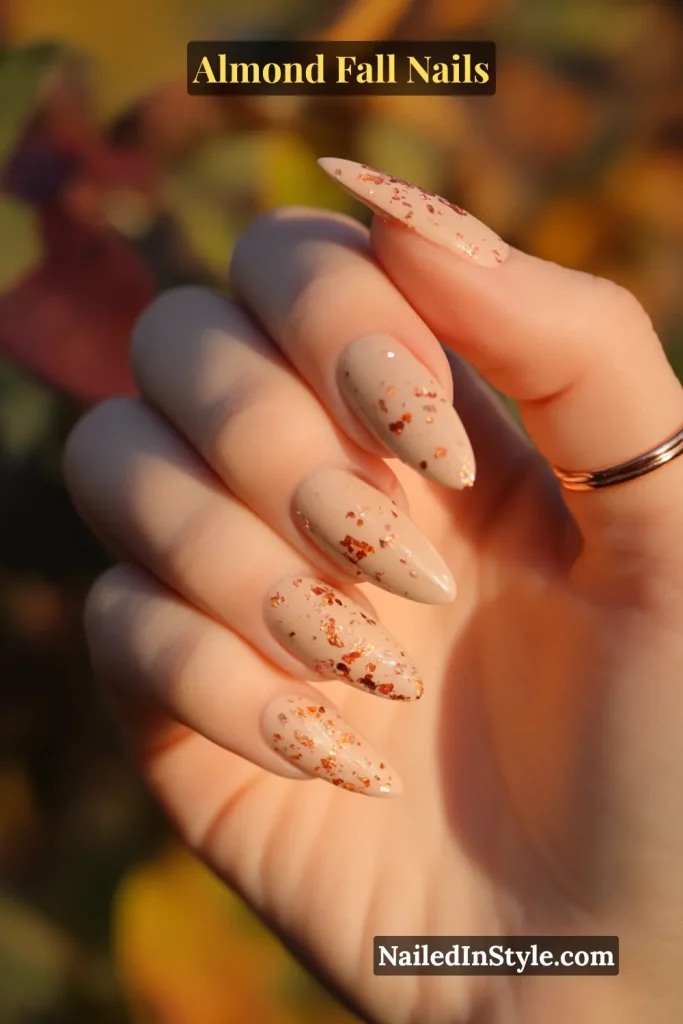 Almond nude nails with glossy finish and copper foil flakes in autumn sunlight.