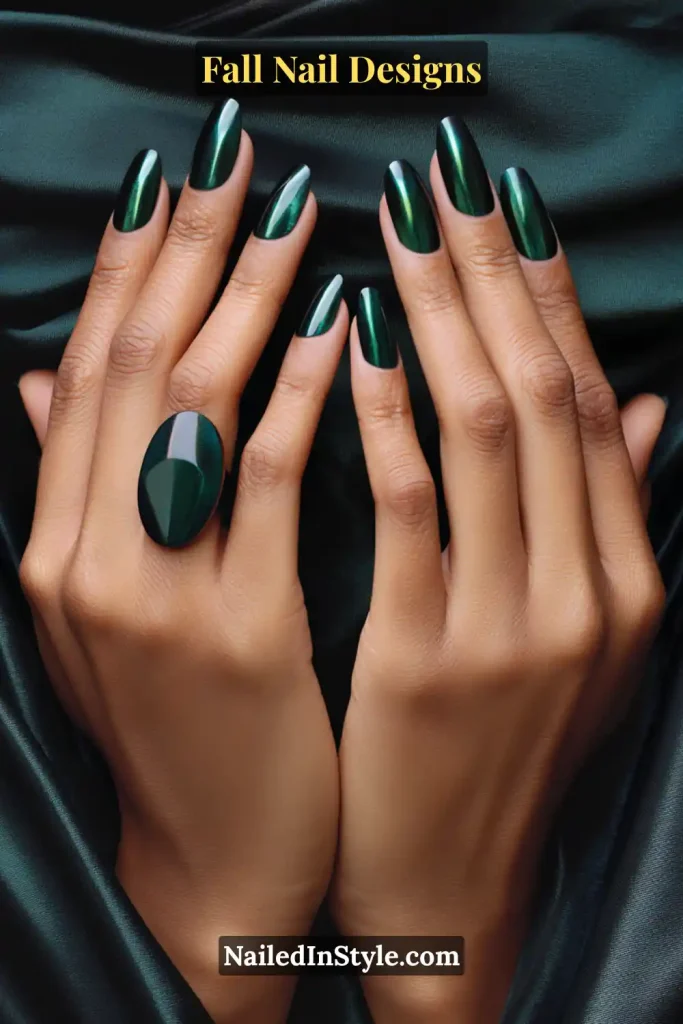 Hands with deep green emerald cat-eye nails and statement ring on satin fabric.