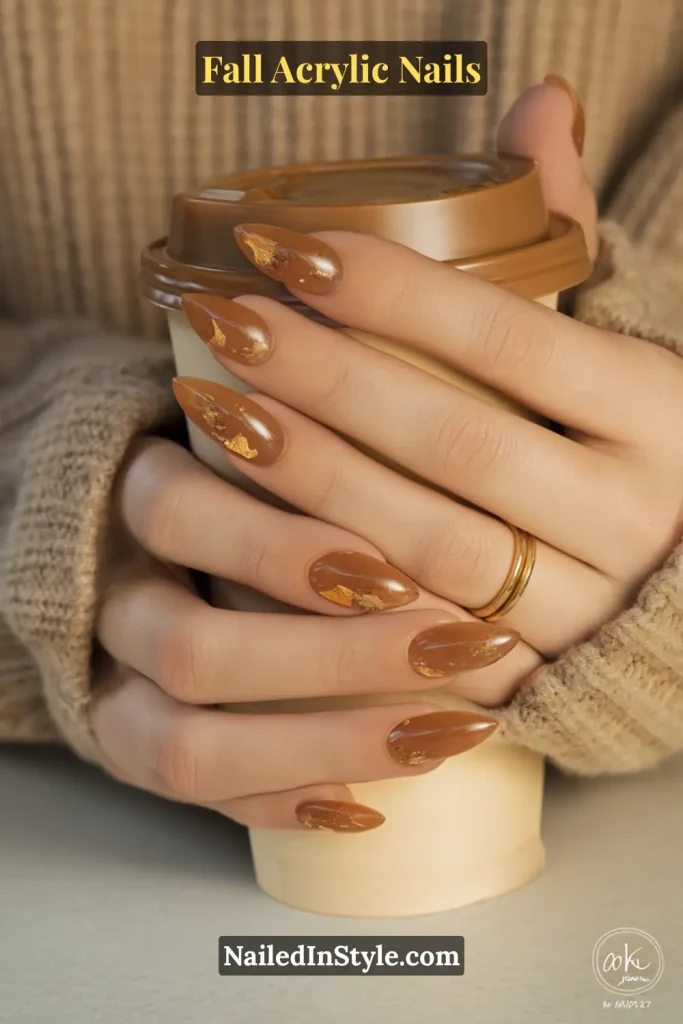 Fall Acrylic Nails Encapsulated almond-shaped acrylic nails with a caramel base and tiny gold leaf flakes on medium olive skin, holding a latte in a ribbed-knit sleeve.