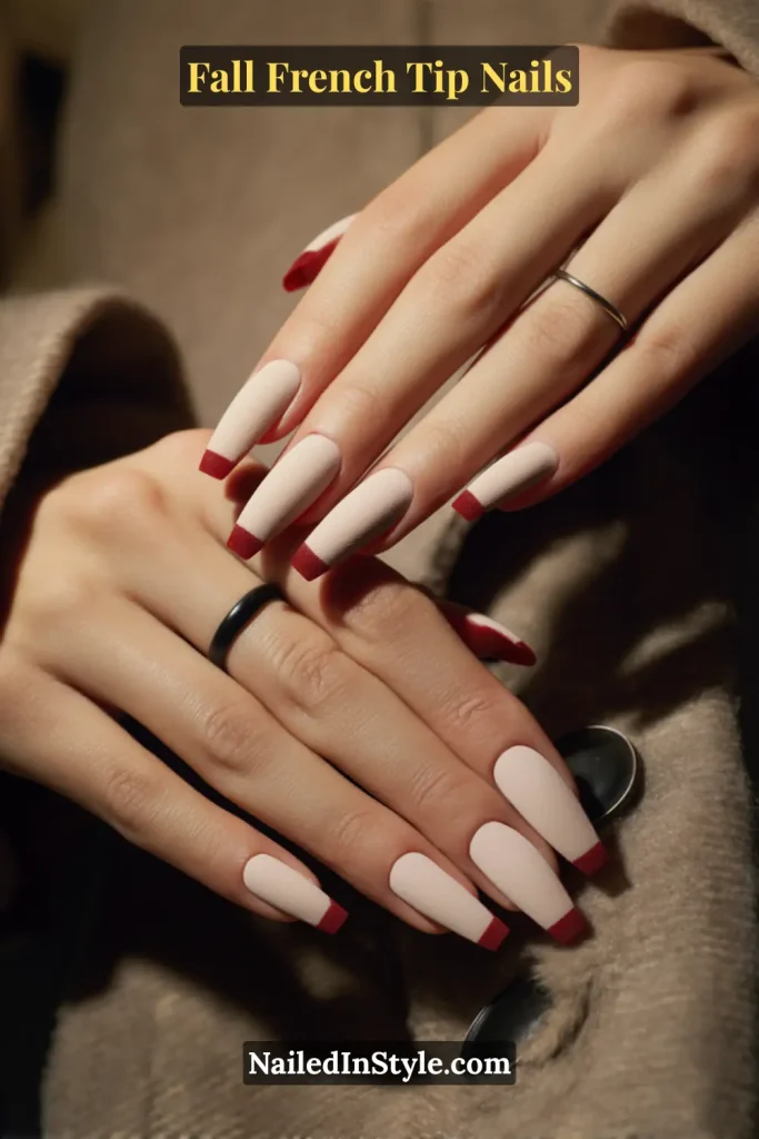 Coffin nails with matte nude base and oxblood red French tips, hands resting on a wool coat with buttons.