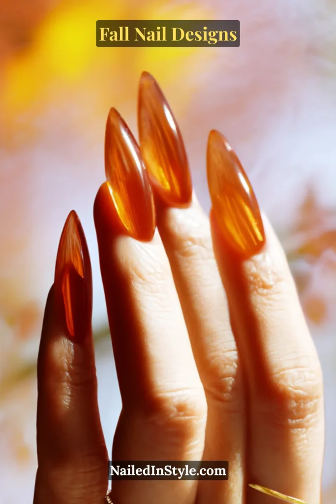 Long stiletto nails in translucent amber jelly finish, hand backlit by window light.