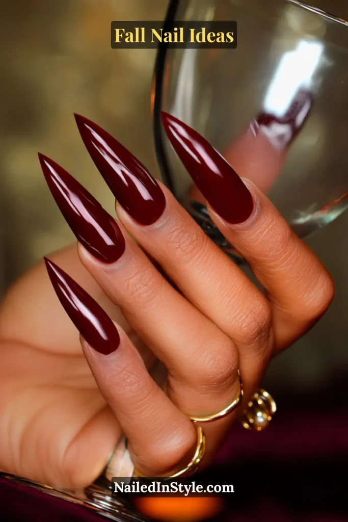 Fall Nail Ideas: 21 Gorgeous Looks to Try Now 7 Long stiletto nails in deep burgundy gloss, hand holding a stemmed glass.