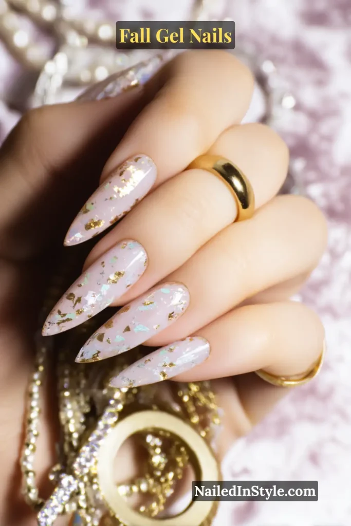 fall gel nails in clear base with scattered gold foil accents, almond shape styled with jewelry pieces for a luxe touch