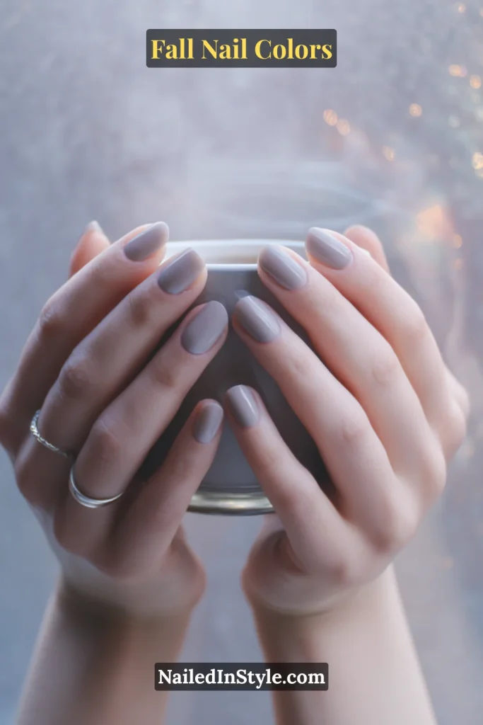 Soft gray nails on fair skin holding a coffee cup against a foggy window, creating a cozy autumn mood.