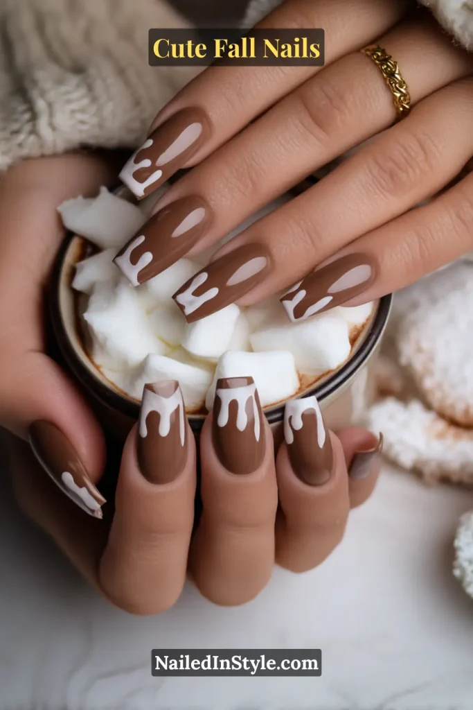 Cute fall nails with glossy chocolate-brown drip designs flowing from the cuticle over a marshmallow white base, styled with a cozy cup of cocoa and marshmallows.
