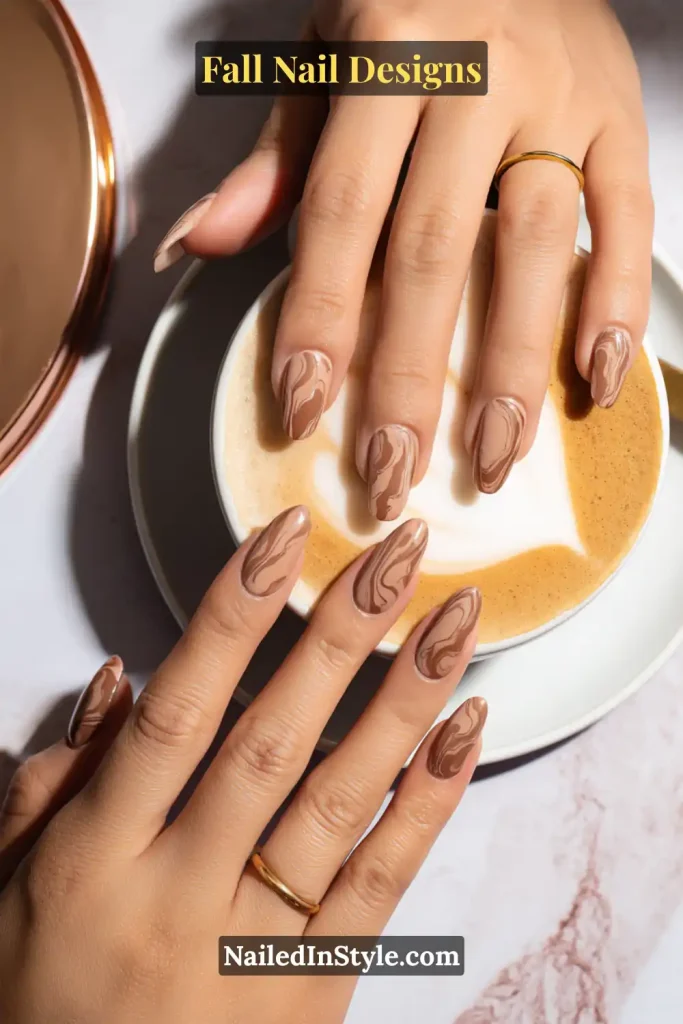 Hands with beige and mocha marble swirl nails holding a latte cup.