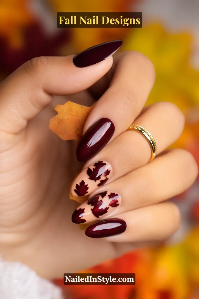 Hand with burgundy and nude nails featuring negative-space maple leaf silhouettes, holding a small maple leaf.
