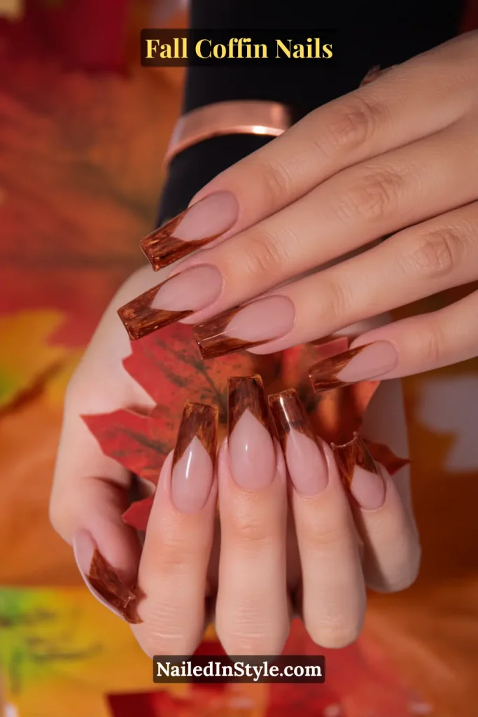 fall coffin nails in maple micro v french style with warm brown tips, holding a maple leaf for a cozy seasonal touch