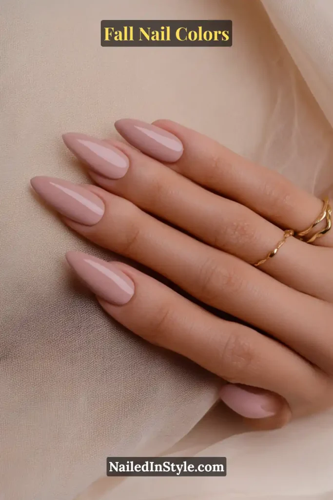 Glossy mauve taupe nails on fair skin styled with minimal gold rings against a soft fabric background.