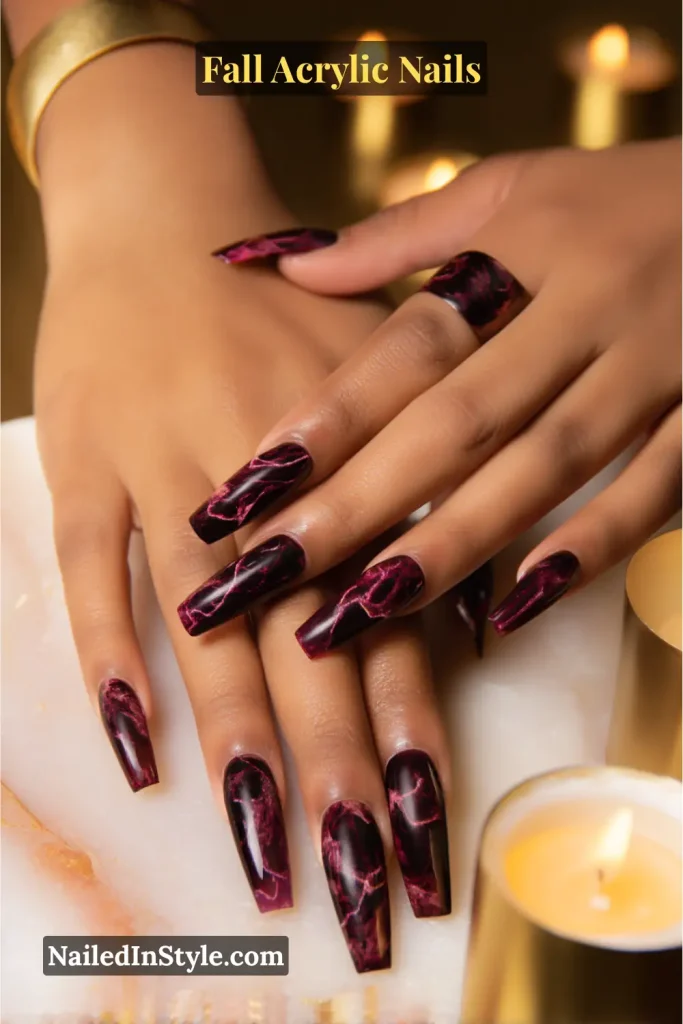 Long coffin acrylic nails in merlot red and black marble smoke design with veined stone effect, displayed over a marble table with glowing candles.