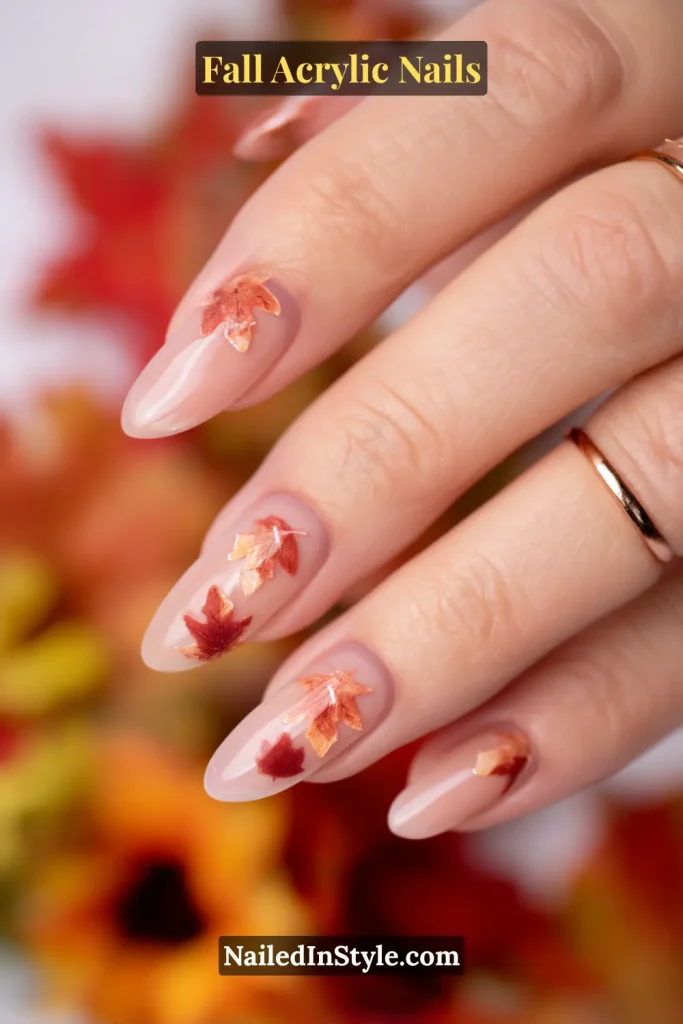 Oval nude acrylic nails with 3D autumn maple leaf embellishments in copper and red tones.