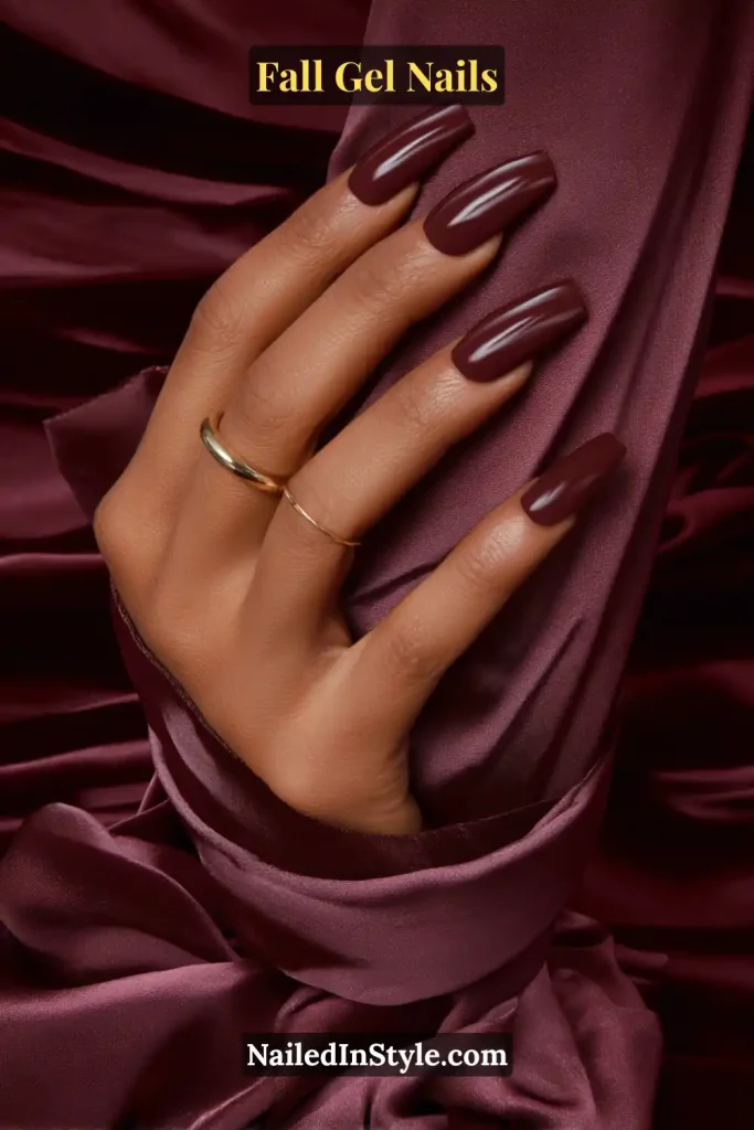 fall gel nails in deep mulberry berry shade with high gloss shine, coffin shape resting on a silk blouse cuff