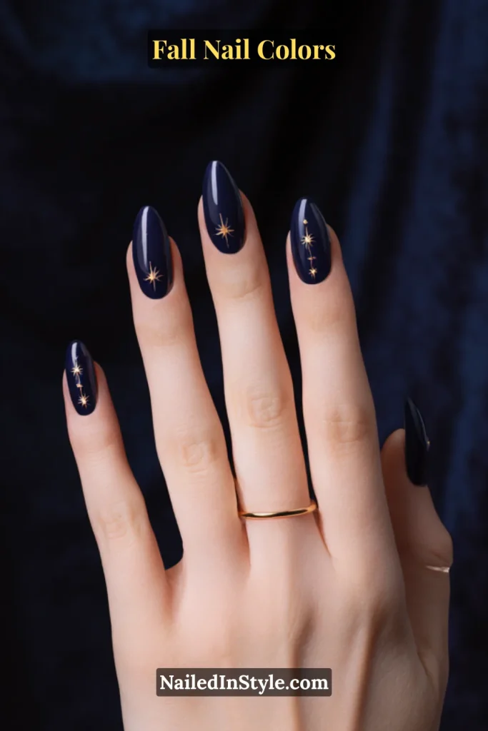 Glossy navy blue nails on fair skin with delicate gold star accents, resembling a midnight sky.