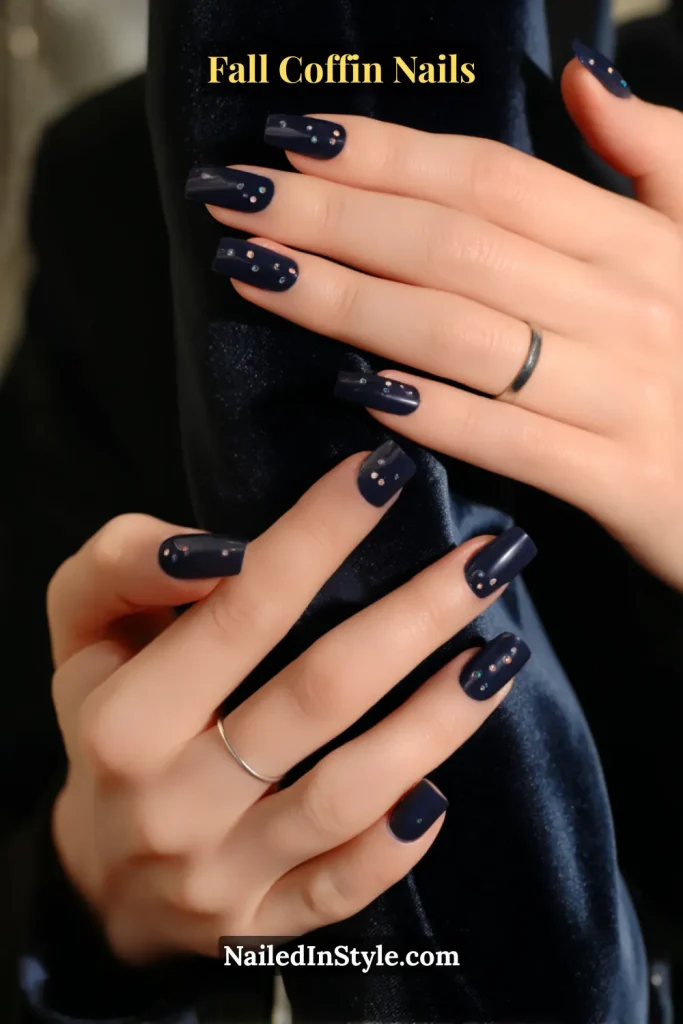 fall coffin nails in midnight navy with tiny star-dot accents near the cuticle, styled against a velvet blazer sleeve
