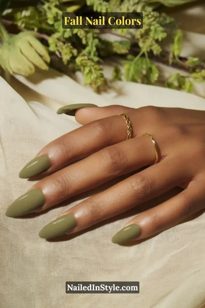 Close-up of almond-shaped nails painted in olive green on medium skin, paired with gold jewelry.