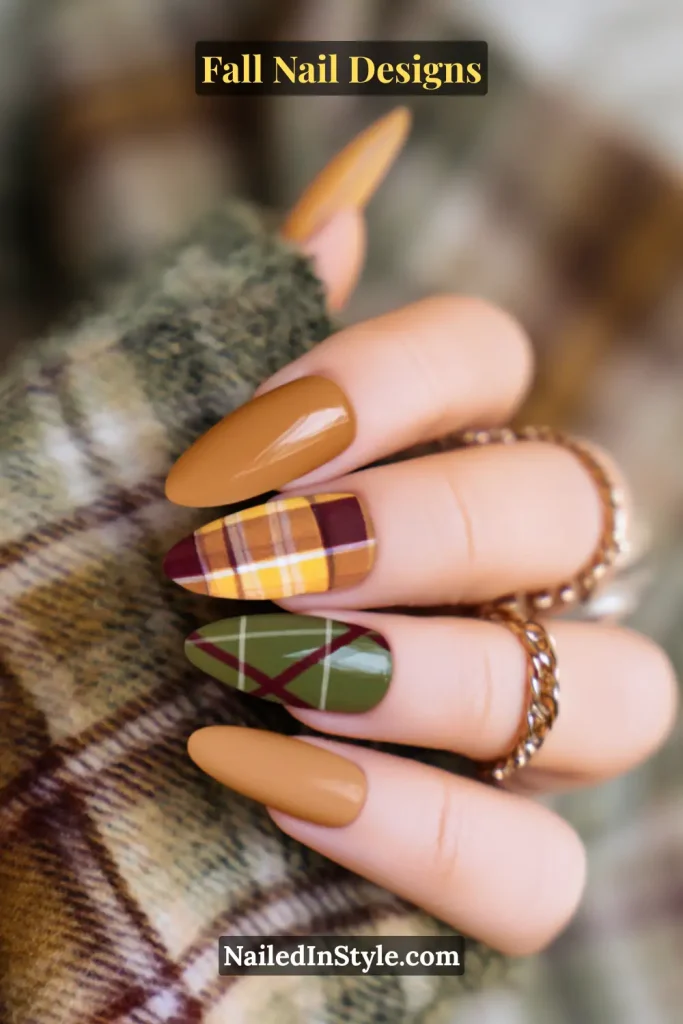 Hand with plaid accent nails in mustard, burgundy, and green against plaid fabric.