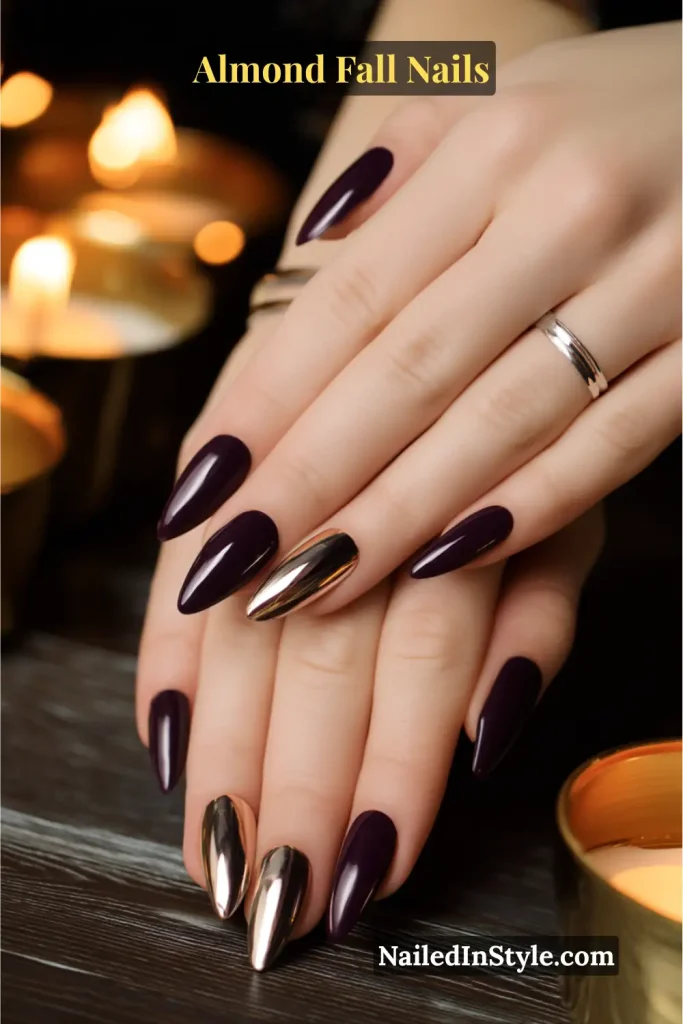 Almond-shaped nails in deep glossy plum with two chrome accent nails, styled on a candle-lit table.