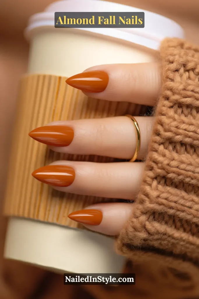 Glossy almond-shaped acrylic nails in warm pumpkin spice orange, holding a latte cup with ribbed-knit sleeve.