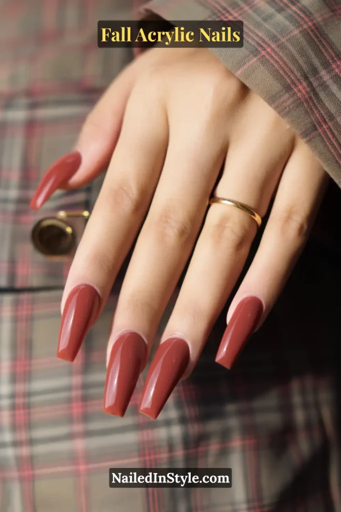Rust red coffin-shaped sculpted French acrylic nails on tan skin, hand resting on a plaid coat lapel with a gold ring.