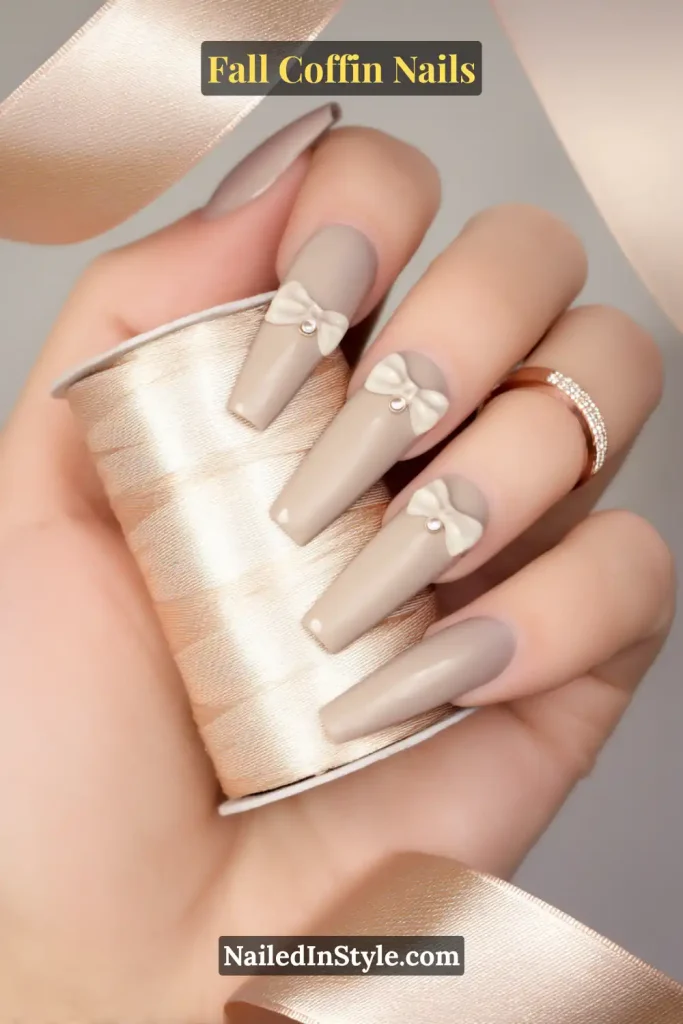 fall coffin nails in taupe with satin bow accents and pearl studs, styled while holding a spool of ribbon