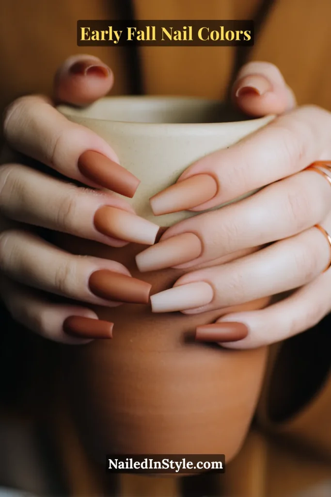 Early fall nail colors in a nude base fading into terracotta tips, styled with hands wrapped around a rustic clay mug.