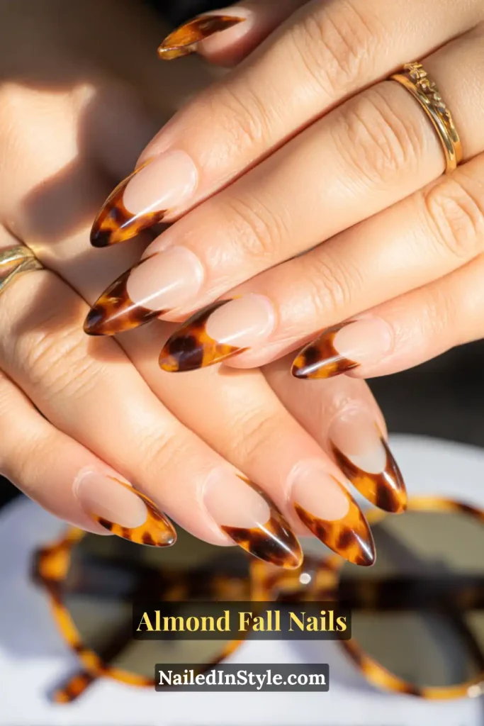 Almond fall nails with a nude base and tortoiseshell French tips, styled with matching tortoise sunglasses.