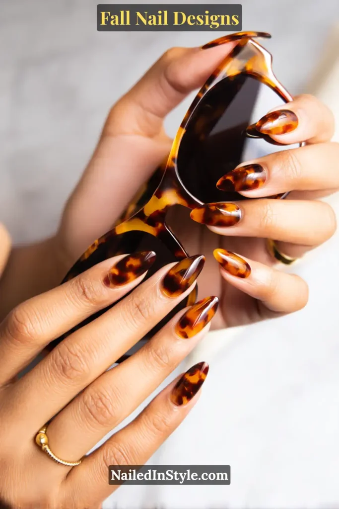 Hands with amber-brown tortoiseshell nails holding tortoise sunglasses.